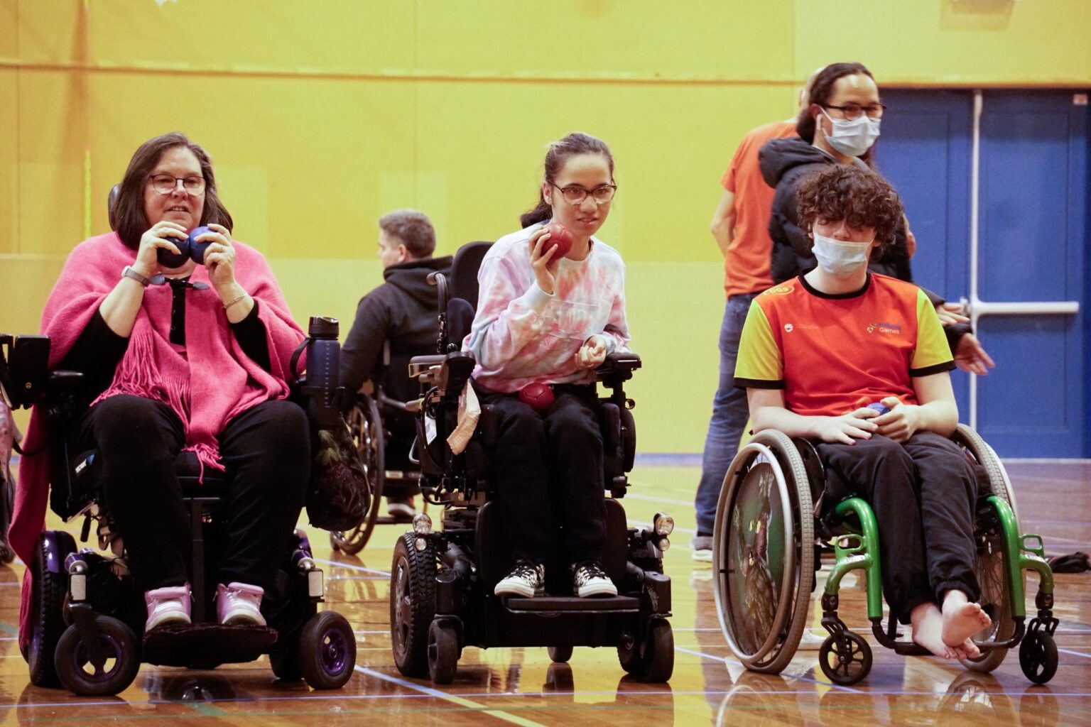 Three people in wheelchairs playing boccia indoors