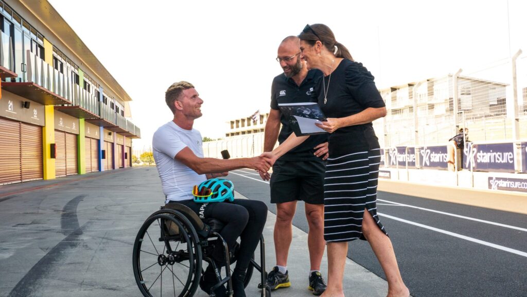 Rory Mead receiving box with pin from coach Damian Wiseman and Deputy Chef de Mission Lynette Grace