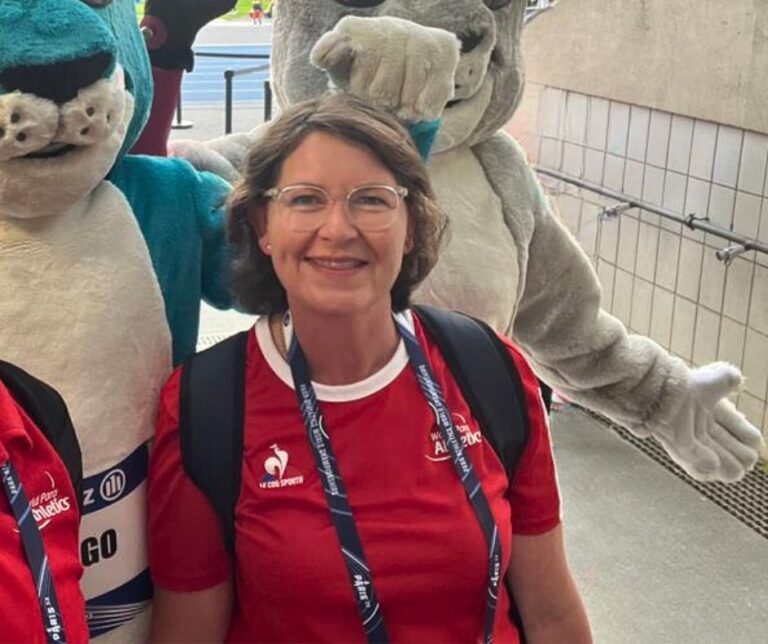 Becs stands with mascots in a stadium