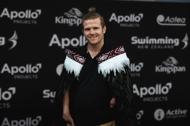 Cameron smiles as he wears a korowai Māori cloak with white feathers along his shoulders