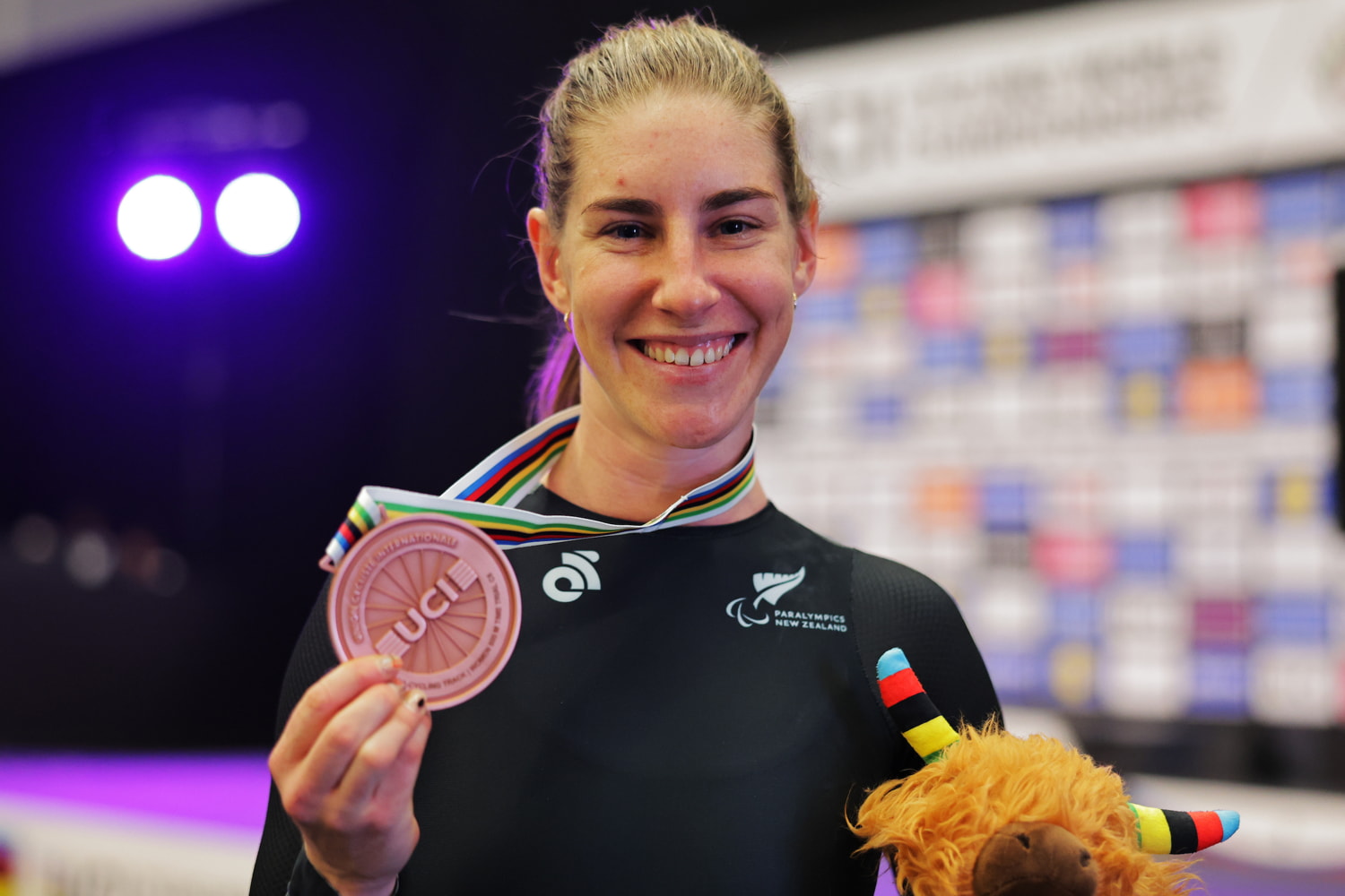 Nicole holds up bronze medal, smiling.