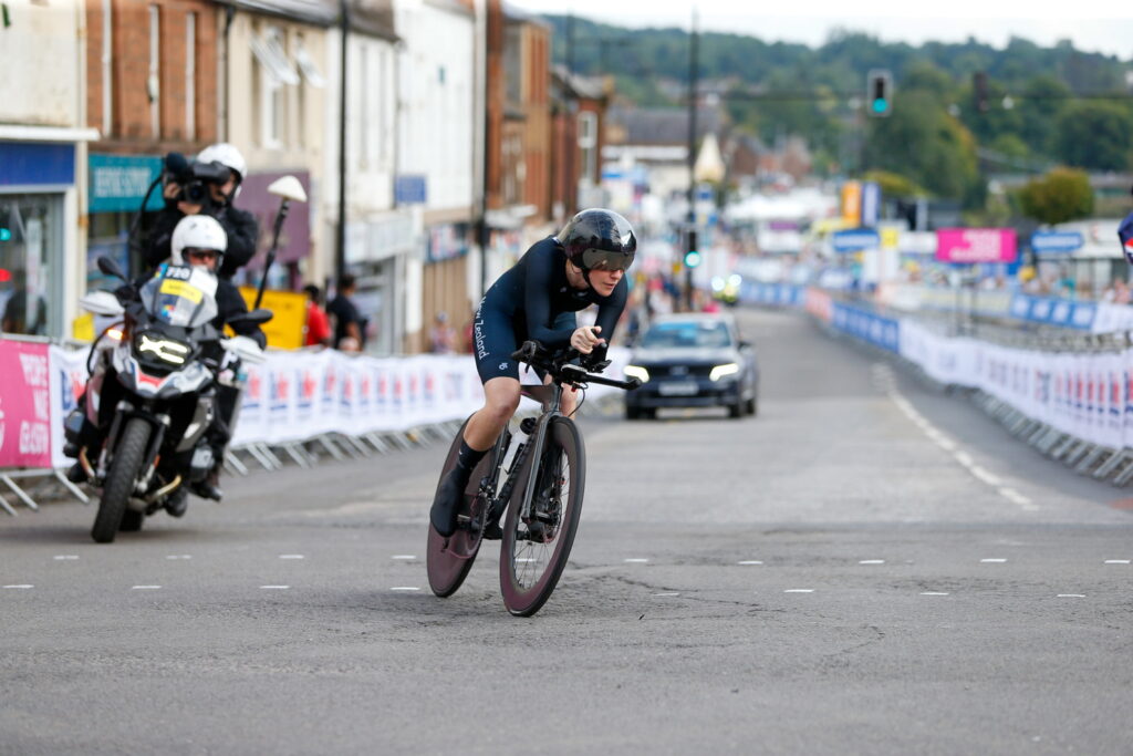 Nicole Murray cycling on road with a camera operator on a motorbike behind her