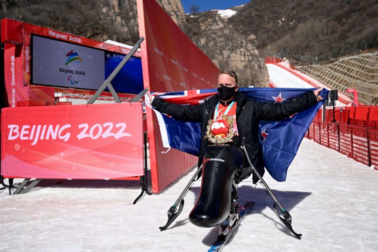 Corey Peters holds out NZ flag at the finish line in Beijing after winning gold medal