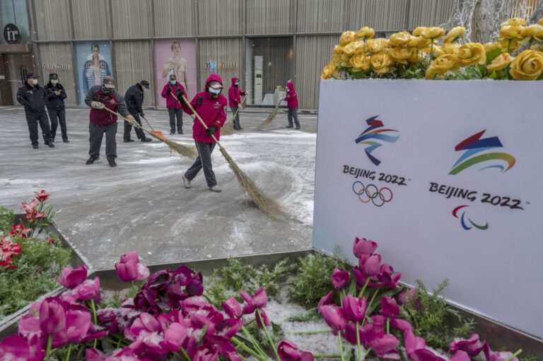 BEIJING, CHINA - JANUARY 20: Volunteers sweep snow next to posters for the Beijing 2022 Winter Olympics and Paralympics, showing mascot Bing Dwen Dwen during a snowfall on January 20, 2022 in Beijing, China.
