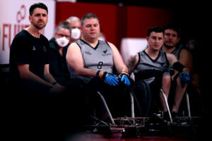 three wheelchair rugby players and their coach wait with concerned faces.