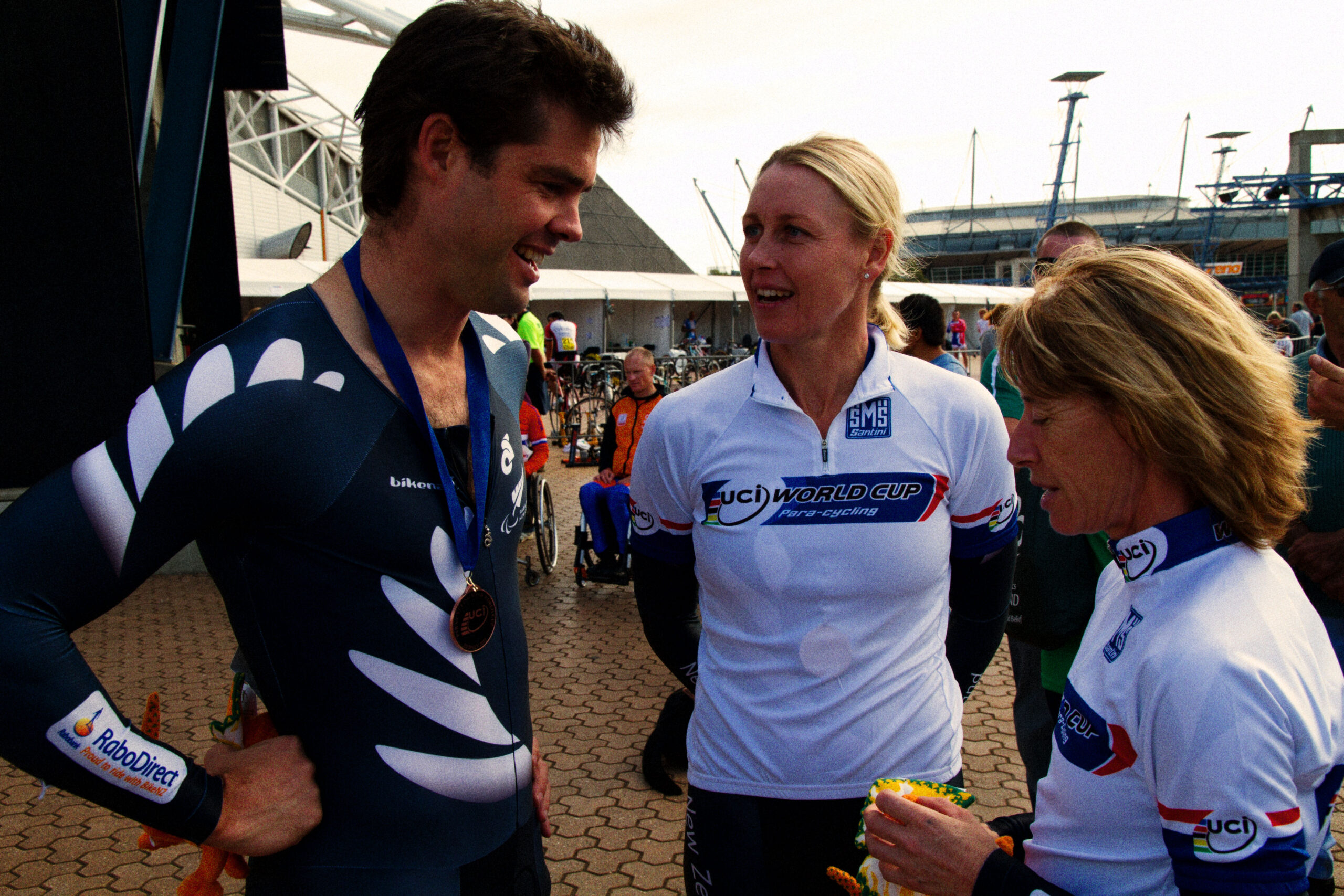 dark haired athlete talking to people after a race wearing cycling gear and a medal