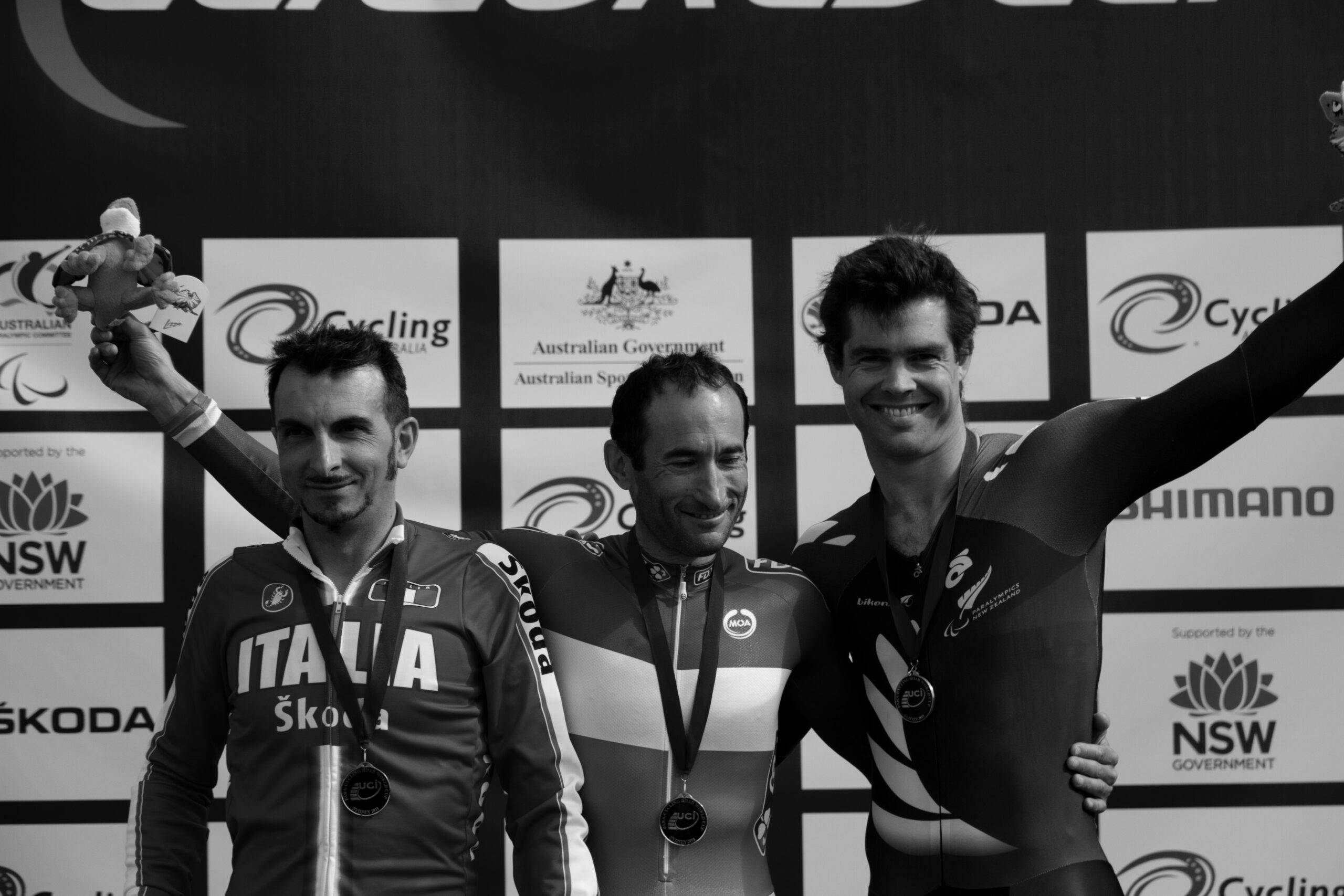 Three men cyclists wave from the podium