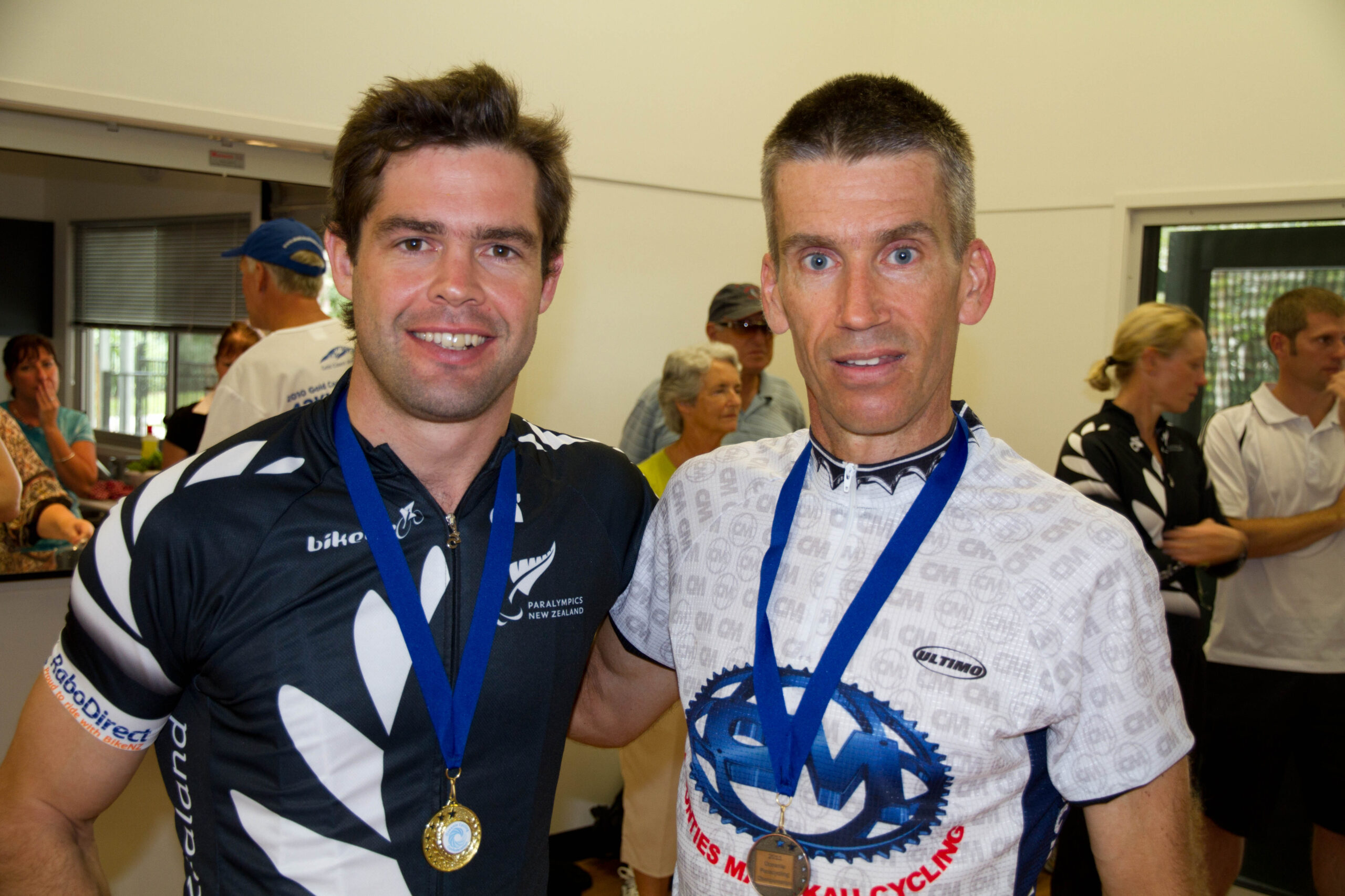Two male cyclists with medals, indoors