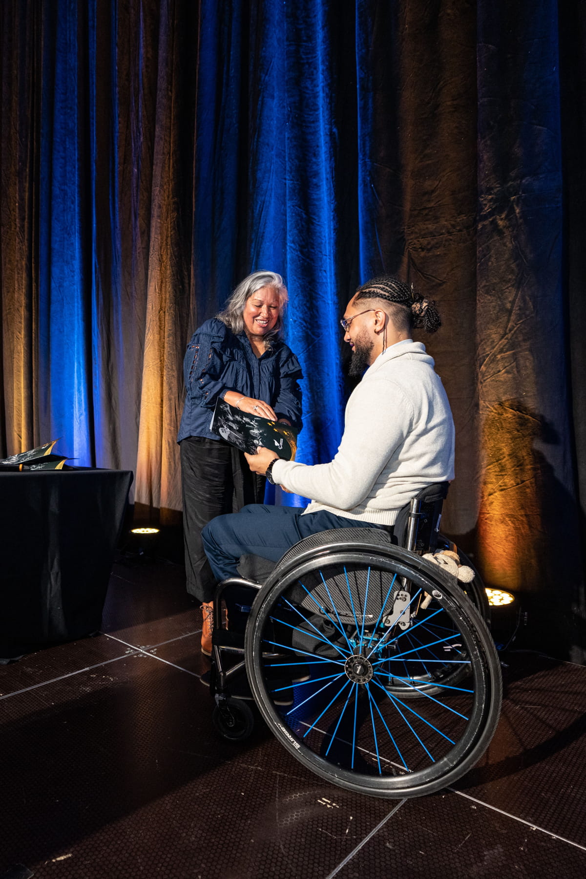 Hayden Barton-Cootes in wheelchair on stage receives pin from Jana Rangooni
