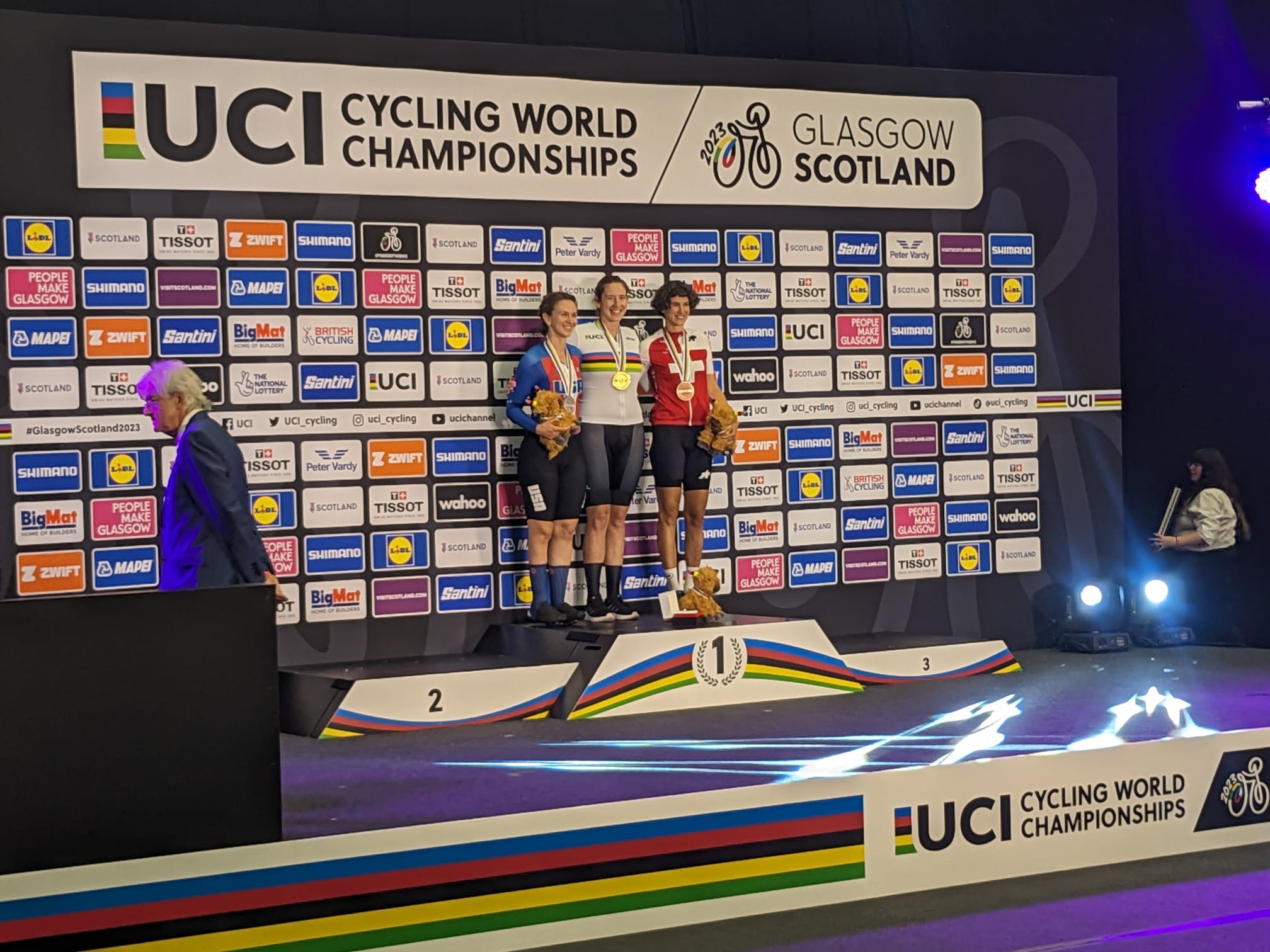 Anna with arms around other medallists on podium wearing rainbows
