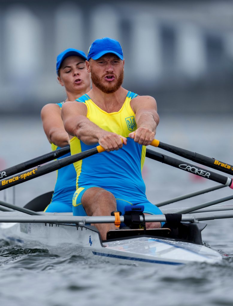 A man and a women wearing blue and yellow rowing powerfully in a boat