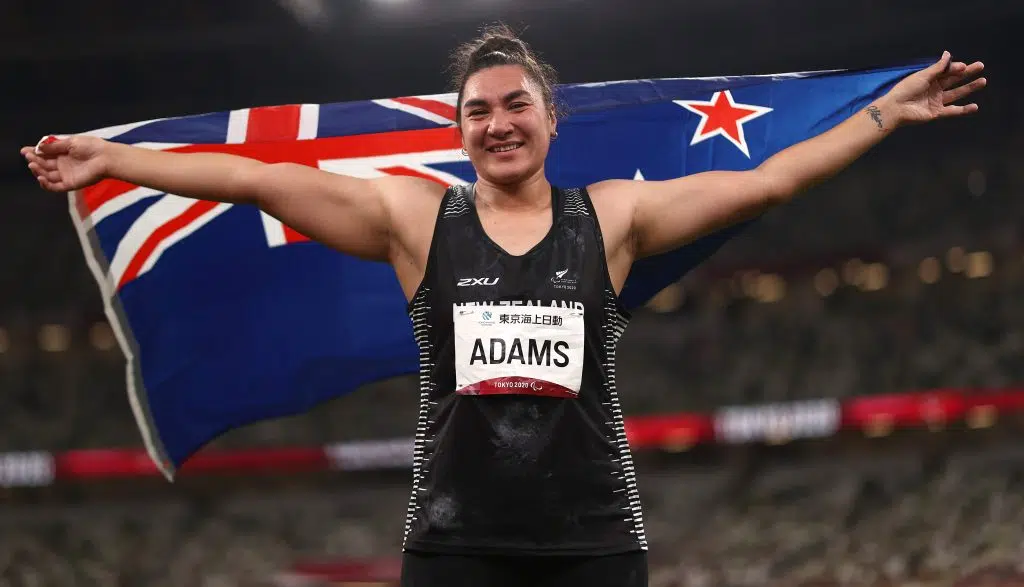 Paralympian Lisa Adams, arms aloft, holding NZ flag at Tokyo 2020 Paralympic Games