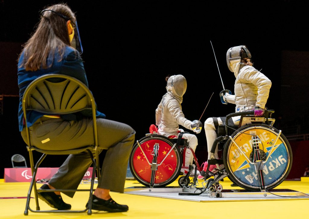 An official watches as fencers in wheelchairs engage in competiton.