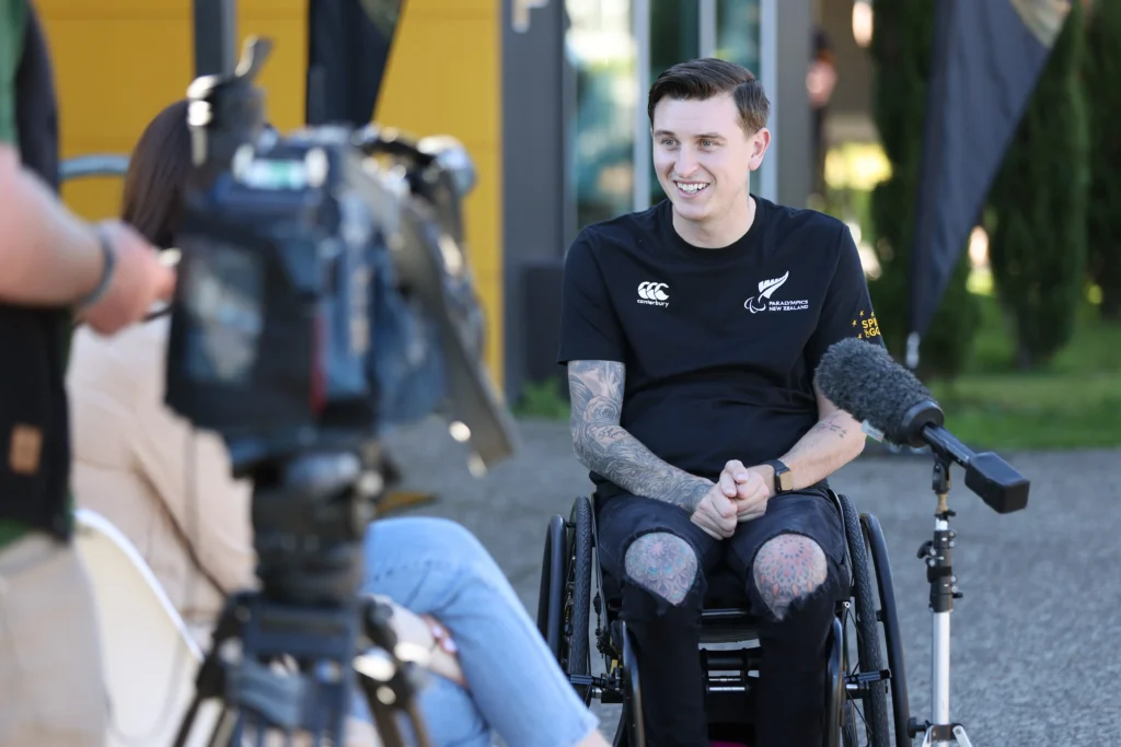 Paralympian Cody Everson in wheelchair being interviewed. Camera and microphone in front of him.