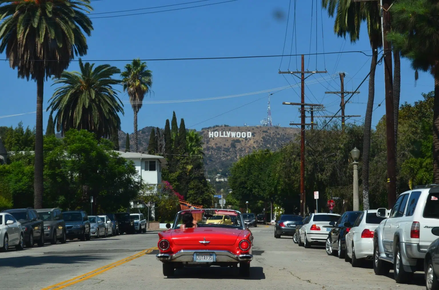 A car on the road with the Hollywood sign in front of it.