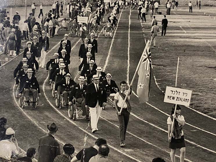 black and white photo of New Zealand in the procession of the Opening Ceremony of Tel Aviv 1968. Most are in wheelchairs and wear white boater hats.