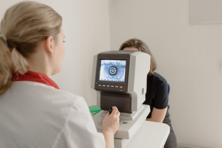 Ophthalmologist looks at the screen of a medical imaging device as a patient sits opposite.