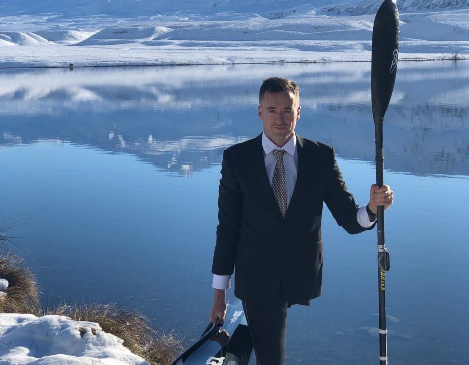 Scott Martlew in business suit holding his canoe and paddle in front of snowy lake