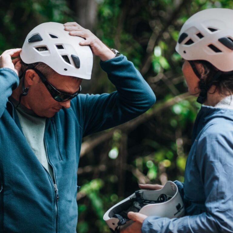 Two people in a forest put on helmets