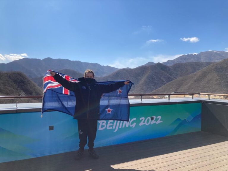 Adam Hall stands with NZ flag in front of Beijing mountains