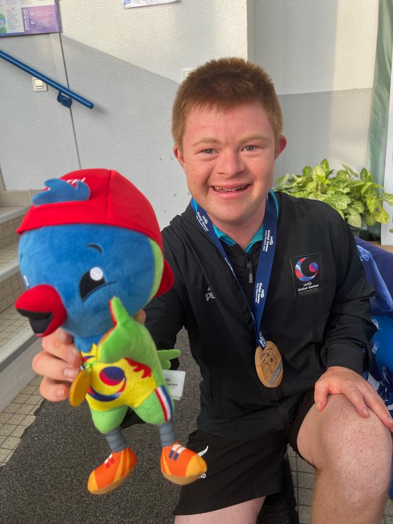 Alfie wears medal and holds up the Virtus mascot, a blue, green and red character