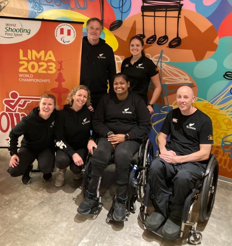 A group of 6 adults wearing black against a colourful backdrop saying "Lima 2023". Two of the people are in wheelchairs.