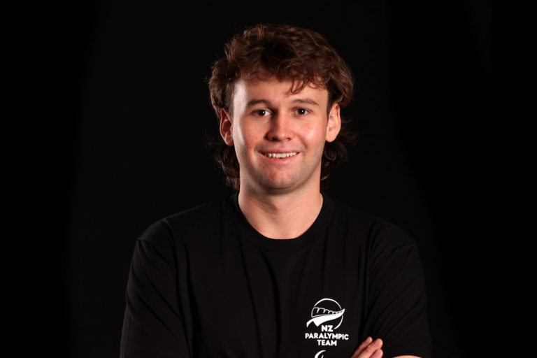 Portrait of Devon Briggs in front of a black backdrop. He wears a black NZ Paralympic Team branded t-shirt.