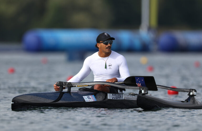 Peter Cowan sits in his kayak after competing in the Men's Va'a Single 200m VL3 Final at the Paris 2024 Paralympic Games. He wears a white long sleeve competition shirt with NZ Paralympic Team branding.