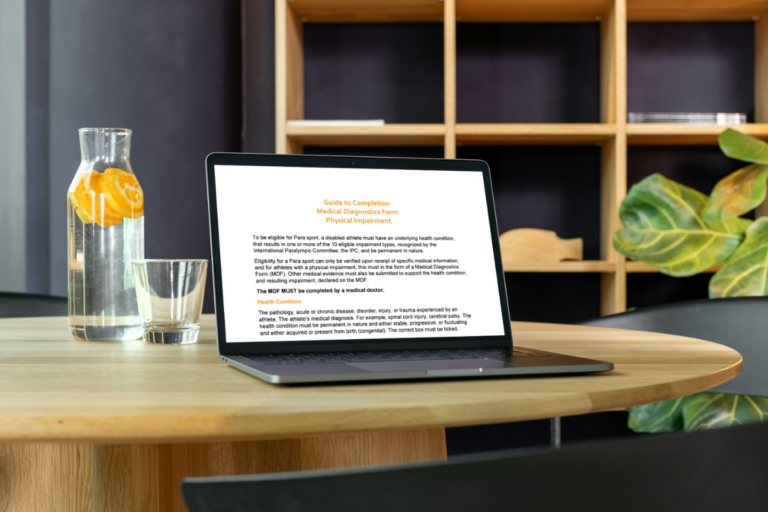 A page of text is visible on a laptop sitting on a table next to a carafe of water