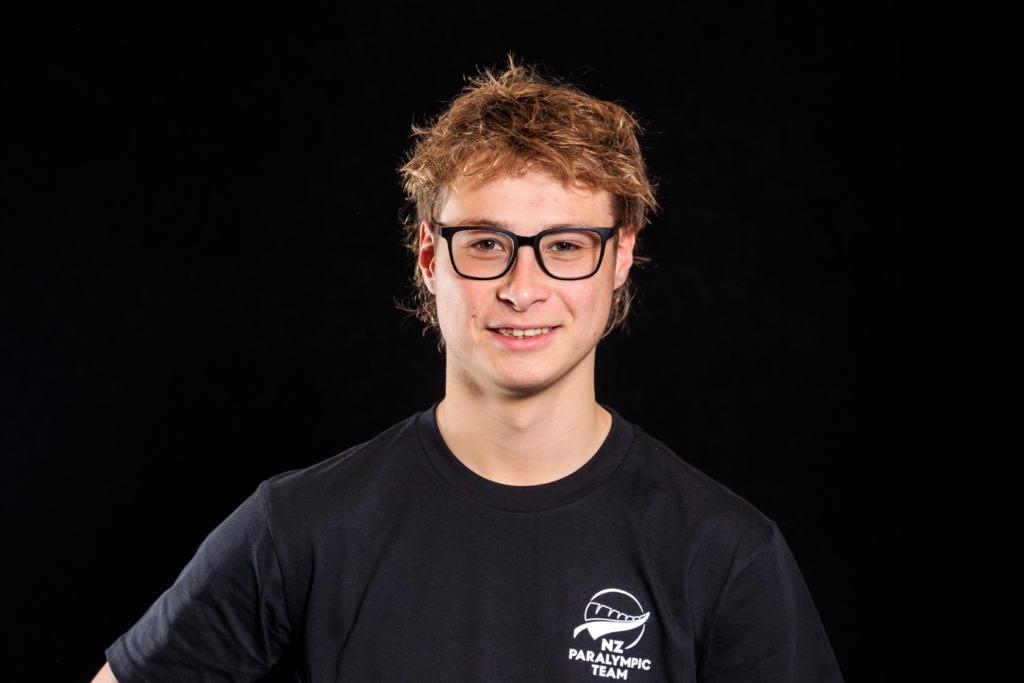 Portrait of Joshua Willmer in front of a black backdrop. He wears a black NZ Paralympic Team branded t-shirt.