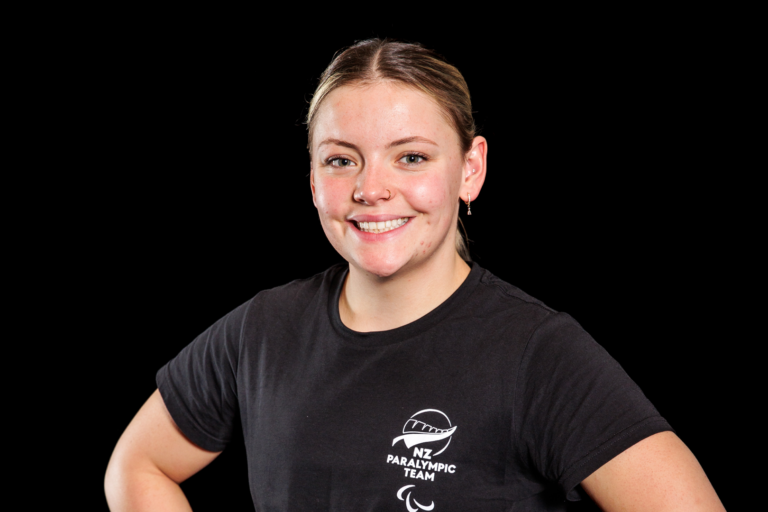 Portrait of Lili-Fox Mason in front of a black backdrop. She wears a black NZ Paralympic Team branded t-shirt.