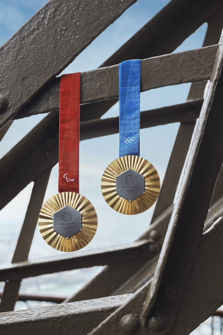 A Paralympic medal with a red ribbon and an Olympic medal with a blue ribbon hang from a strut of the Eiffel Tower