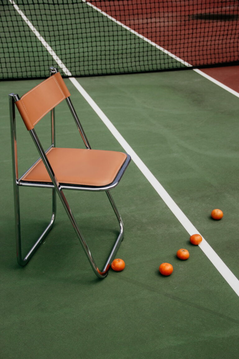An empty folding chair on a tennis court, with a few oranges lying nearby