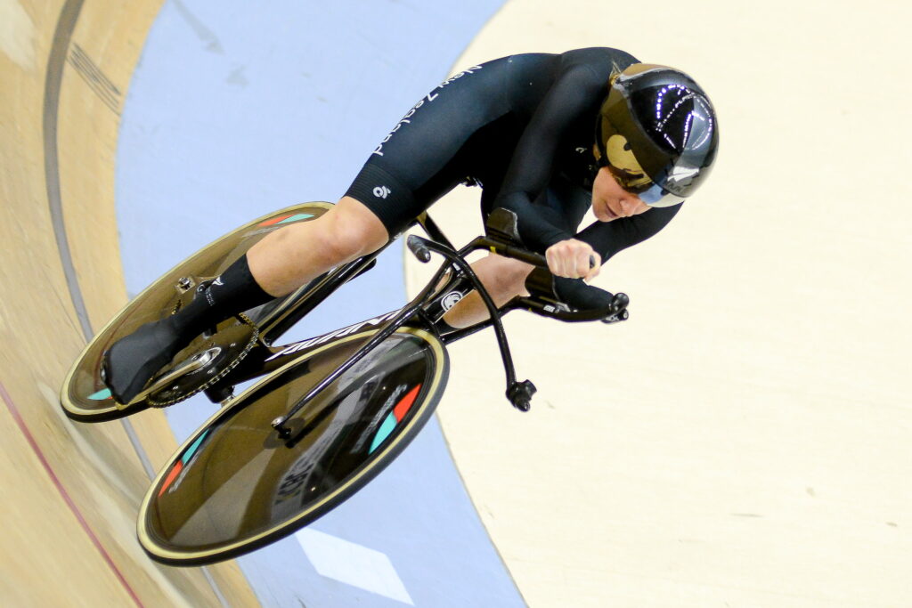 Nicole wears a black skinsuit and looks almost horizontal as she races around the track