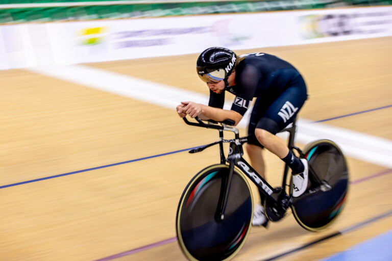 Devon is cycling fast on the track, hunched over his bike