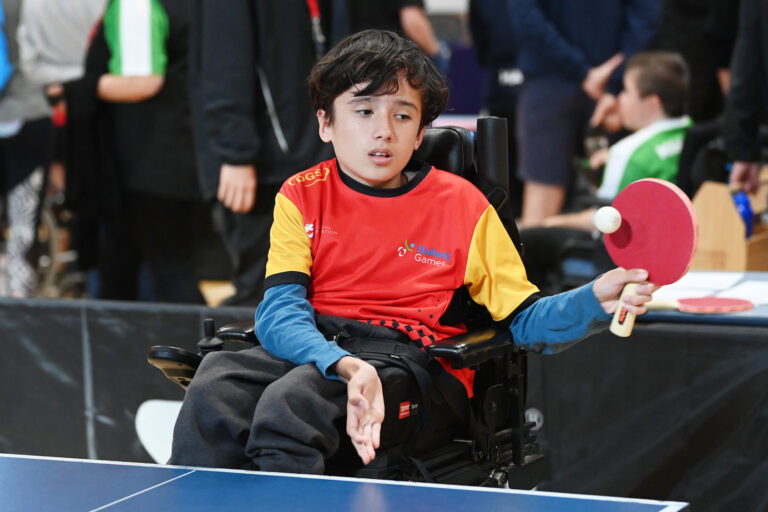A boy using a wheelchair serves the ball in a game of table tennis