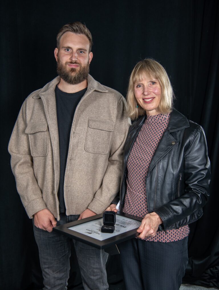 A young man and a middle-aged woman, both light skinned and fair haired are holding a certificate in this professional portrait