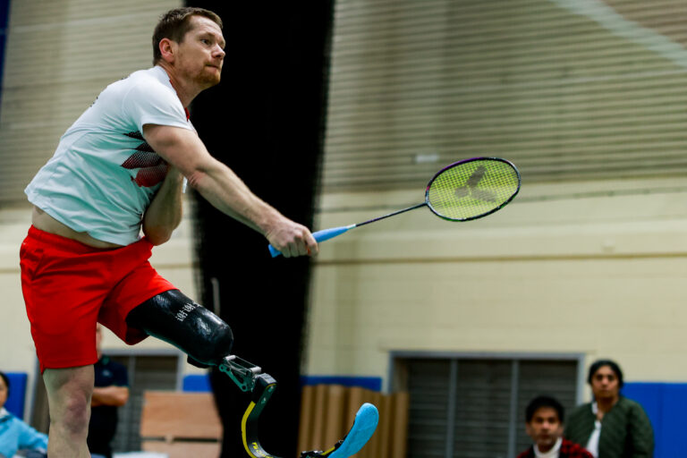 male wearing light blue tshirt and red shorts swings badminton racket