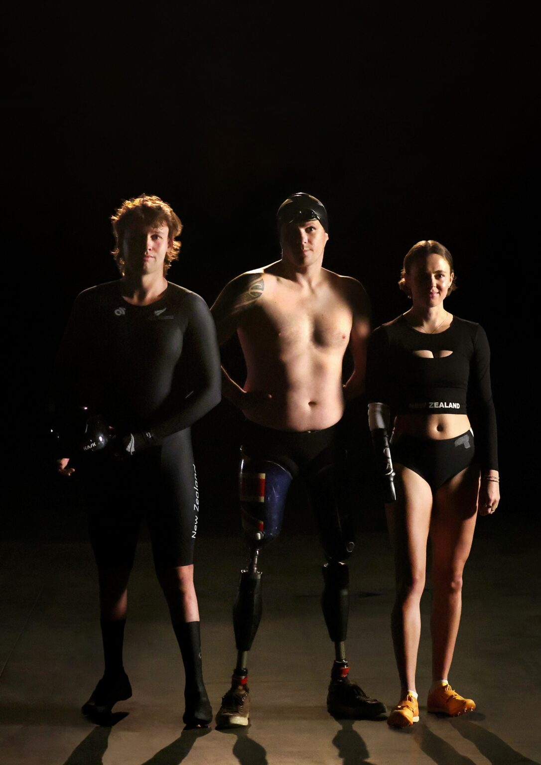 Two men and a woman stand together in front of a black background. All three are wearing sports apparel