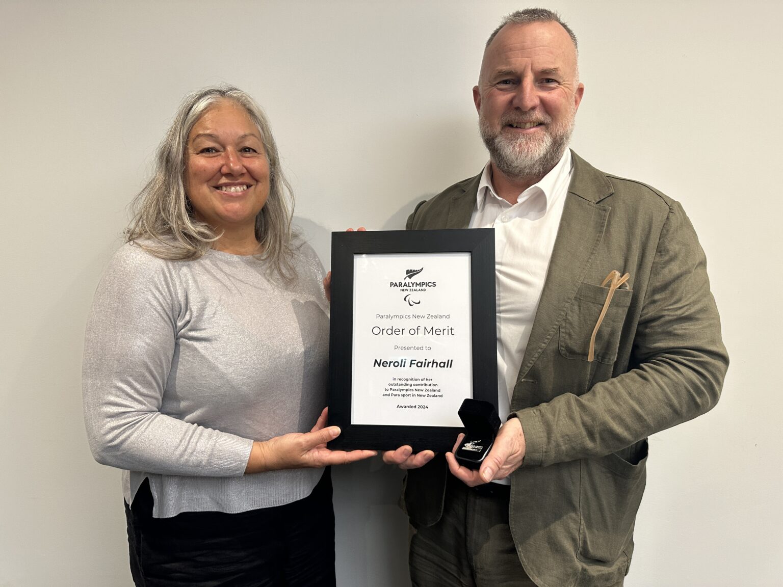 A female presents a male with a framed certificate. Both are smiling towards camera