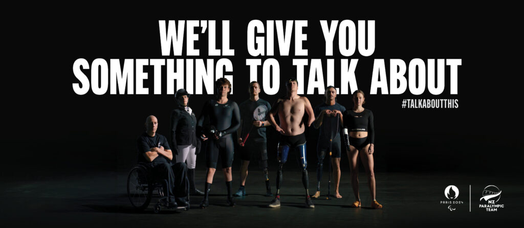 Big bold white text reads "We'll give you something to talk about" with 7 Paralympians and Para athletes underneath. From left to right, Michael Johnson #148, Louise Duncan, Devon Briggs, Wojtek Czyz, Cameron Leslie #164, Peter Cowan and Anna Grimaldi #195. Black backdrop with Paris 2024 and NZ Paralympic Team logos in bottom right.