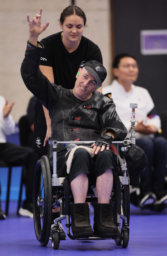 Michael Johnson in wheelchair with arm raised. A Woman behind him in black tshirt.