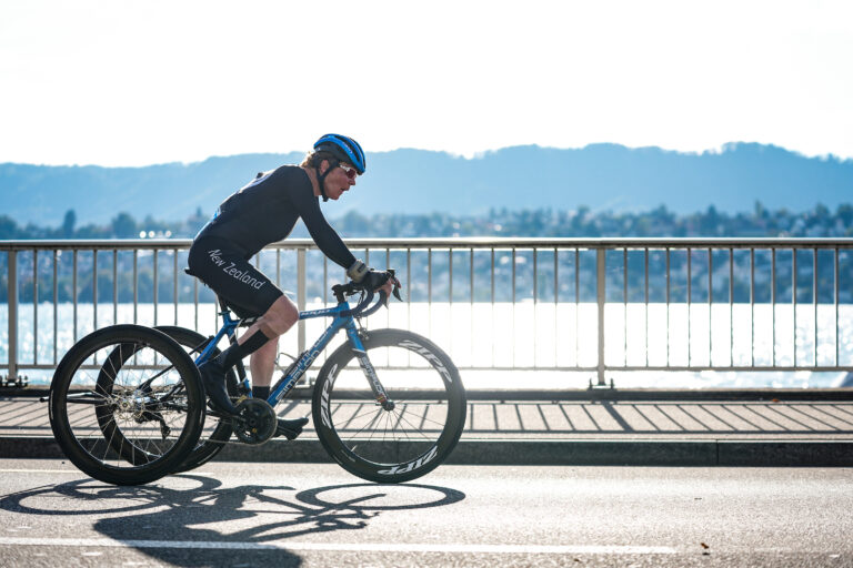 Paralympian #220 Eltje Malzbender cycles across a Zurich bridge spotlighted by the sun at the 2024 UCI Para cycling world championships.