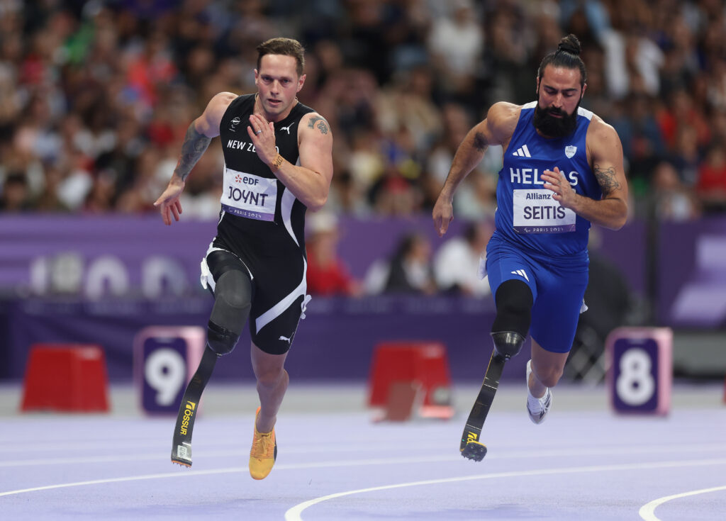 Mitch Joynt and Michail Seitis (Greece) compete during the Men's 200m T64 Final. Both Paralympians are sprinting on a purple track and have a prosthetic on the right leg.