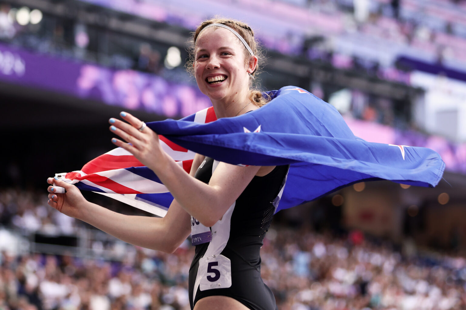 Danielle Aitchison holds the NZ flag around her shoulders as she celebrates her silver medal in the Women's 100m T36 at the Paris 2024 Paralympic Games.