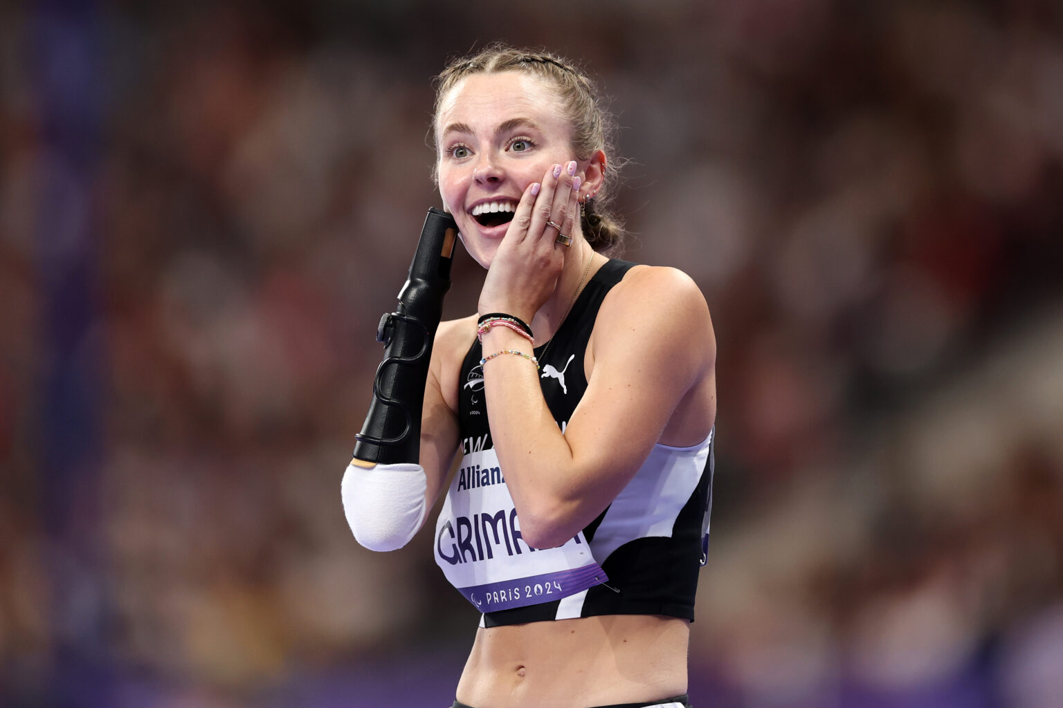 Anna Grimaldi holds her face in surprise as she wins bronze in the Women’s 100m T47 at the Paris 2024 Paralympic Games. Her prosthetic forearm cover is visible on her right arm.