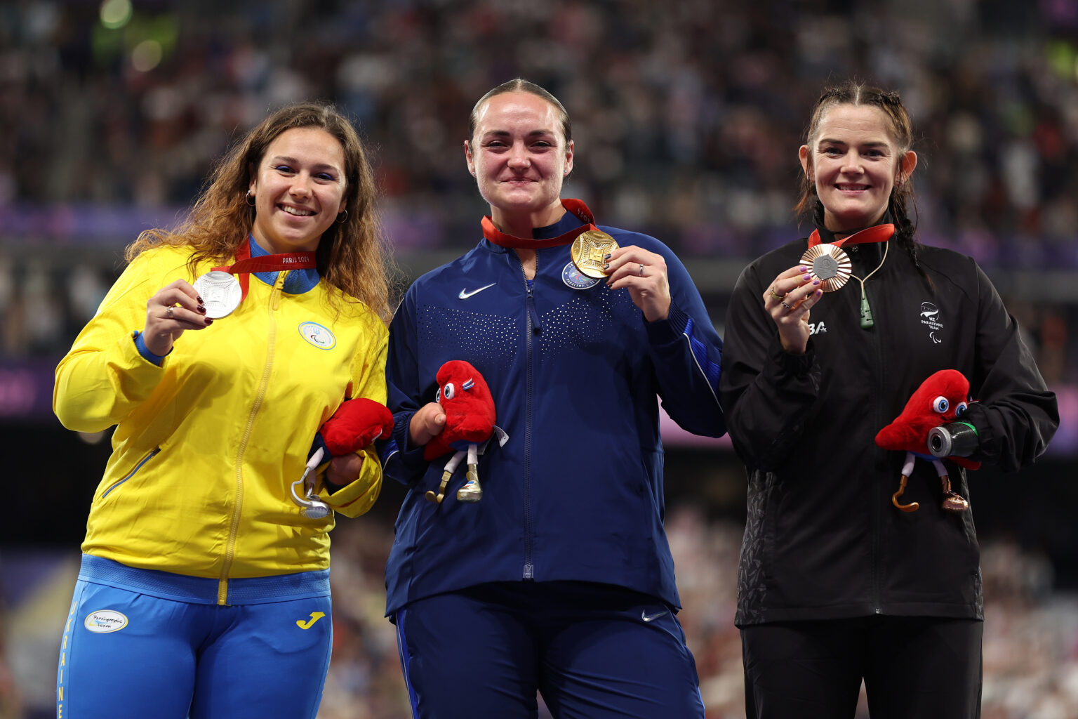 Holly Robinson holds her bronze medal alongside Silver medalist Mariia Shpatkivska and Gold medalist Noelle Malkamaki during the medal ceremony for Women's Shot Put F46 Final at the Paris 2024 Paralympic Games.