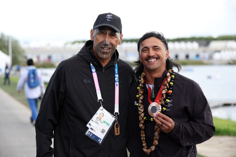 Paralympian Peter Cowan holds his bronze medal following the Men's Va'a Single 200m VL3 Final at the Paris 2024 Paralympic Games. He stands with his coach Myka Nuku.