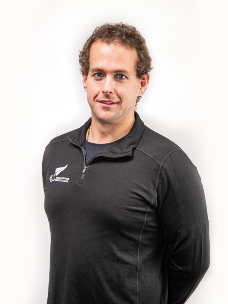 Formal portrait of Paralympian Adam Hall infront of a white background. He wears a Paralympics New Zealand shirt.