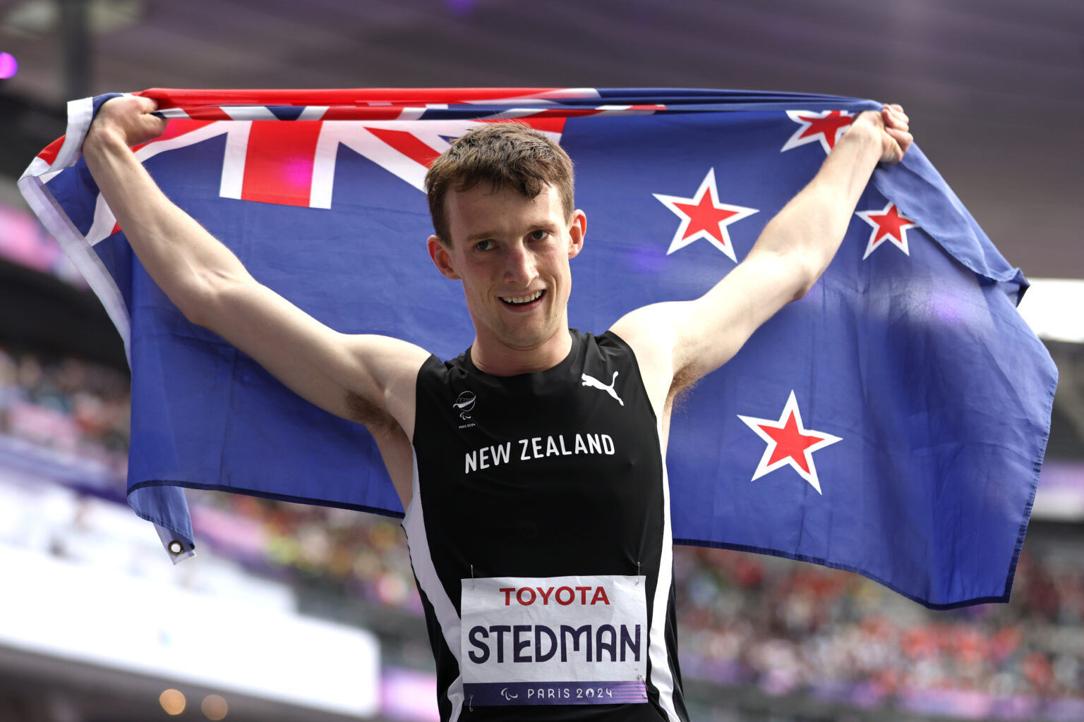 Paralympian #208 William Stedman holds the NZ Flag in his arms at the Paris 2024 Paralympic Games